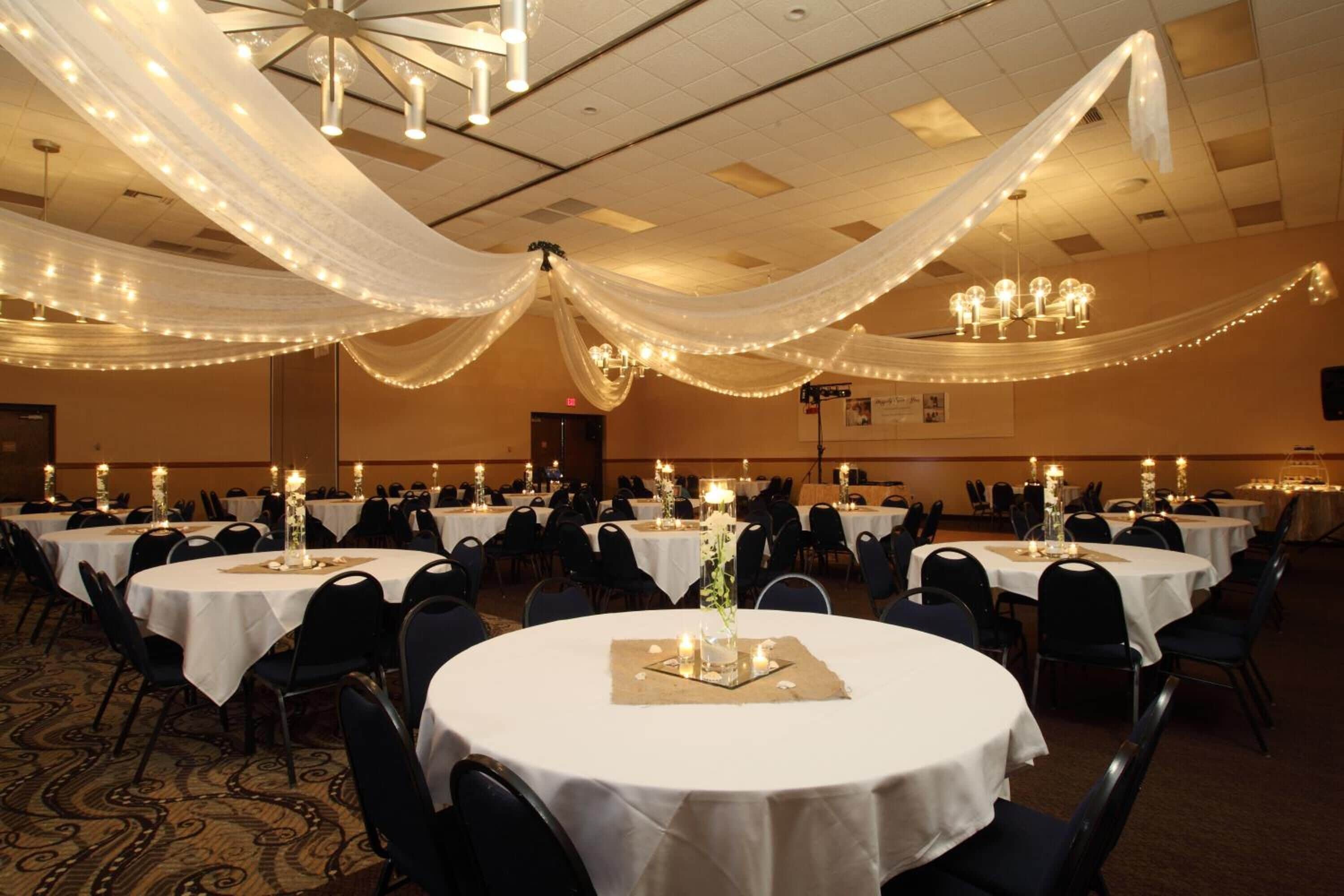 A banquet hall with round tables, white tablecloths, and chandeliers.