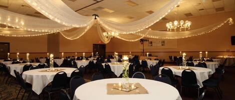 A banquet hall with round tables, white tablecloths, and chandeliers.