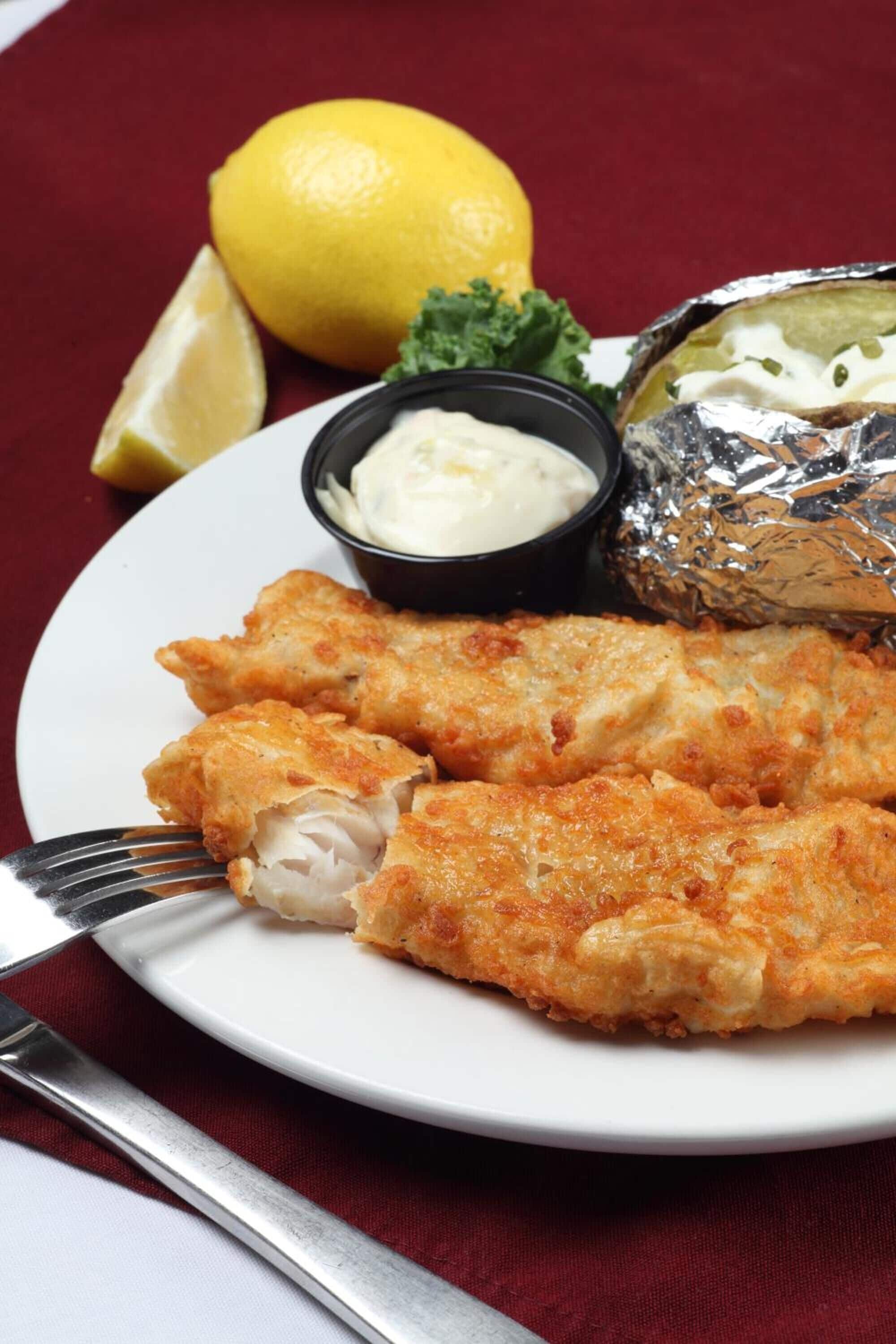 A plate with breaded fish fillets, lemon wedges, and a small bowl of sauce.