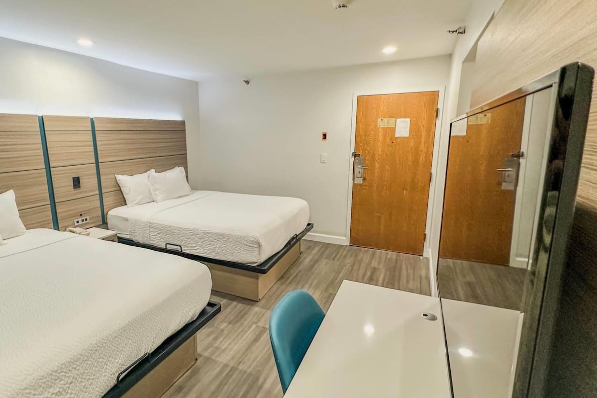 A hotel room with two beds, a desk, a chair, and a mirror.