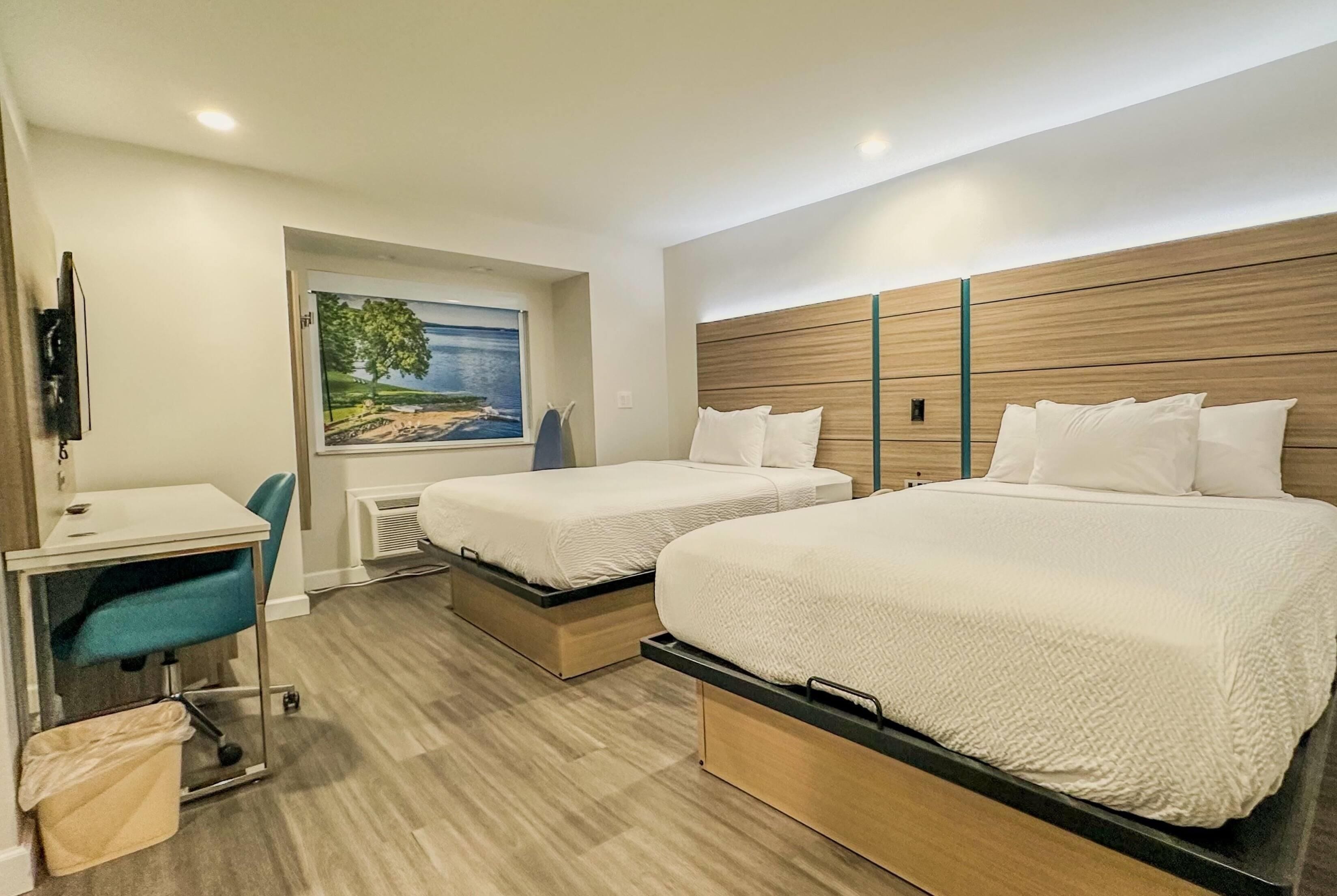 A hotel room with two beds, a desk, a chair, and a painting of a landscape.