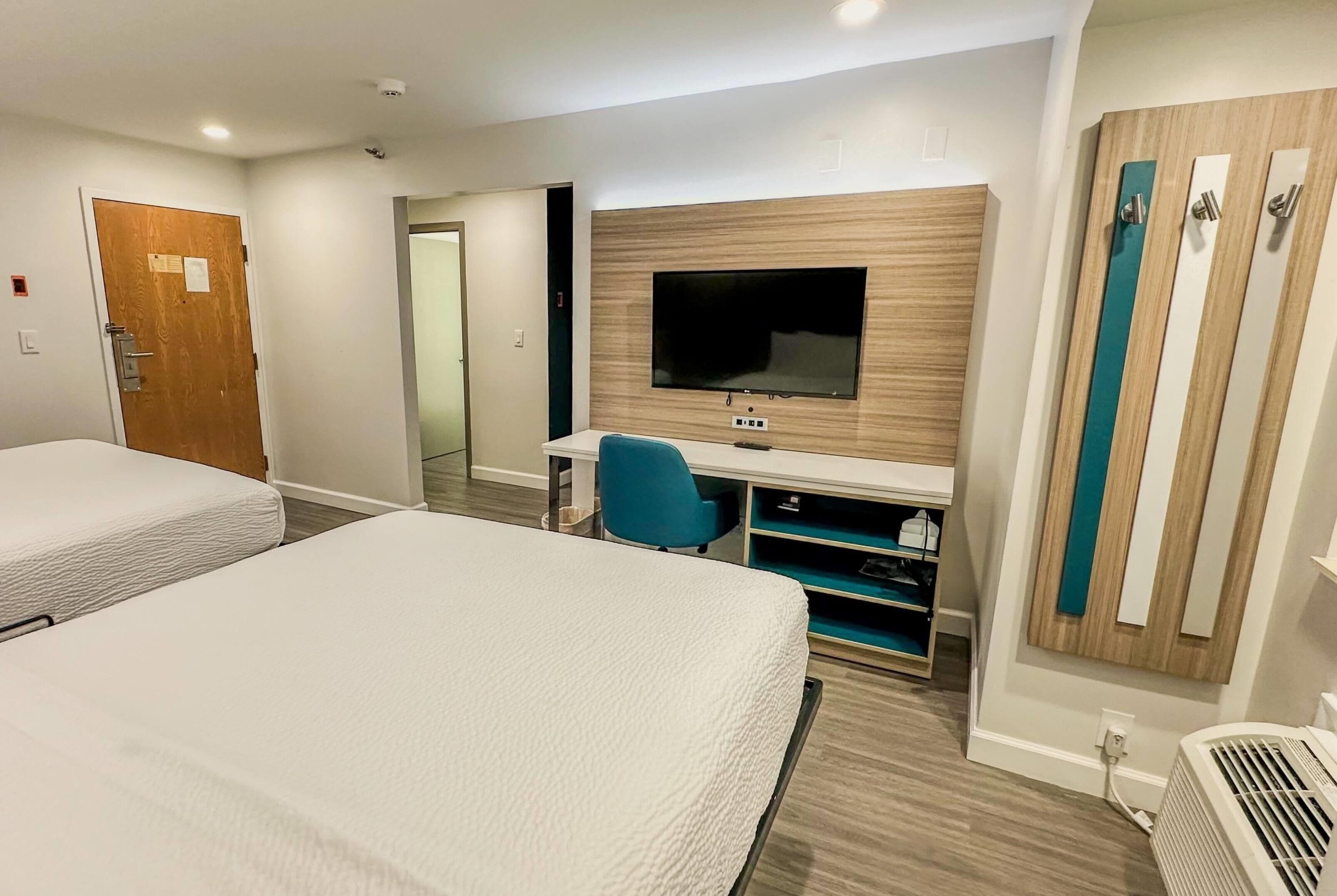 Une chambre d’hôtel avec deux lits, un bureau avec une télévision et une armoire.