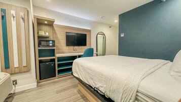 Habitación de hotel con cama, escritorio con computadora, televisor, microondas, espejo y armario.