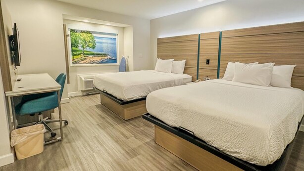 A hotel room with two beds, a desk, and a chair. There is a painting on the wall and a window with a view. - Baymont by Wyndham Henrietta/Rochester (Henrietta)