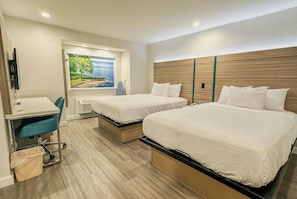 A hotel room with two beds, a desk, and a chair. There is a painting on the wall and a window with a view.