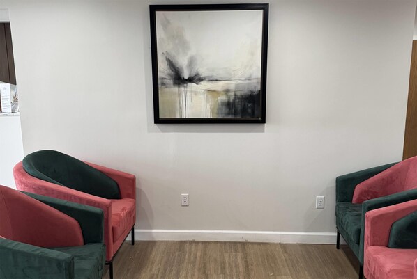 A room with a large abstract painting on the wall, two green and red chairs, and a wooden floor.