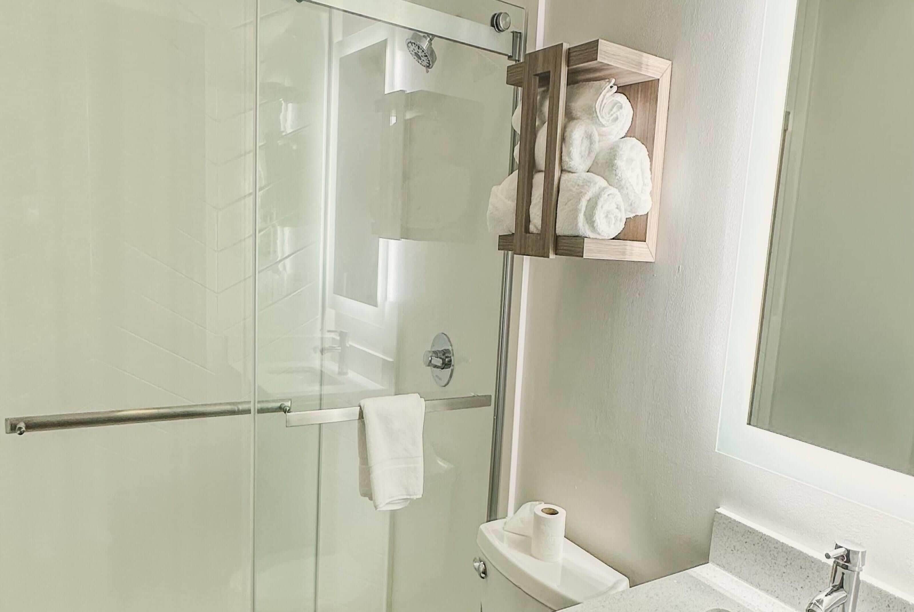 Un baño con cabina de ducha de vidrio, toallero de madera, inodoro y lavamanos.