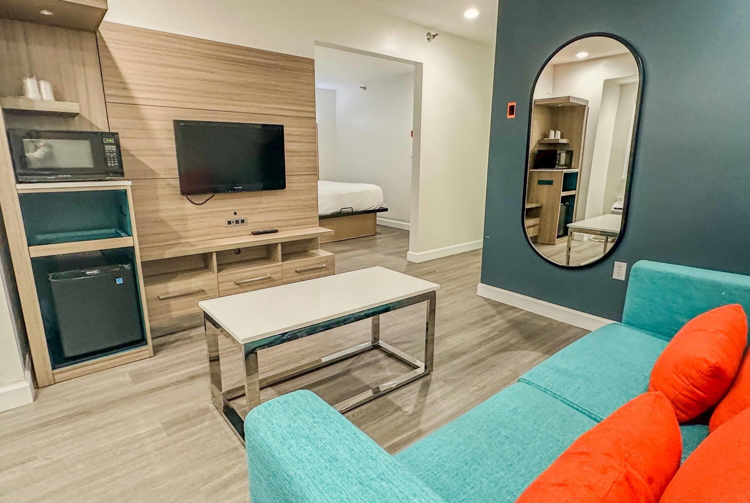 A compact living space with a kitchenette, a flat-screen TV, a bed, and a mirror.