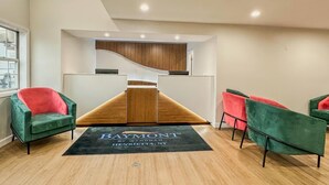 A modern reception area with a wooden reception desk, green and red chairs, and a black carpet with the hotel name. - Baymont by Wyndham Henrietta/Rochester (Henrietta)