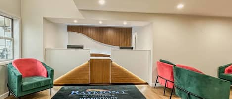 A reception area with a modern design, featuring a wooden reception desk, green and red chairs, and a black carpet with text.