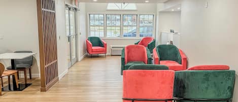A modern interior with a wooden floor, a dining area with a table and chairs, and a seating area with red and green upholstered chairs.