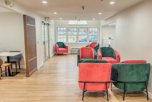 Um interior moderno com piso de madeira, uma área de refeições com mesa e cadeiras, e uma área de estar com poltronas estofadas em vermelho e verde.