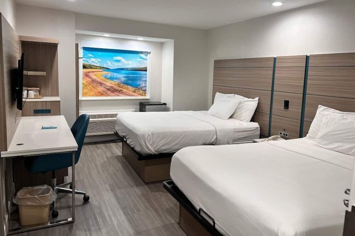 A hotel room with two beds, a desk, a TV, and a large window with a scenic view.