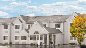 A row of white buildings with a covered entrance and a tree with yellow leaves. - Baymont by Wyndham Henrietta/Rochester (Henrietta)