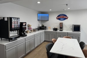 Espaço de café da manhã com máquina de café, micro-ondas, torradeira e uma TV na parede.