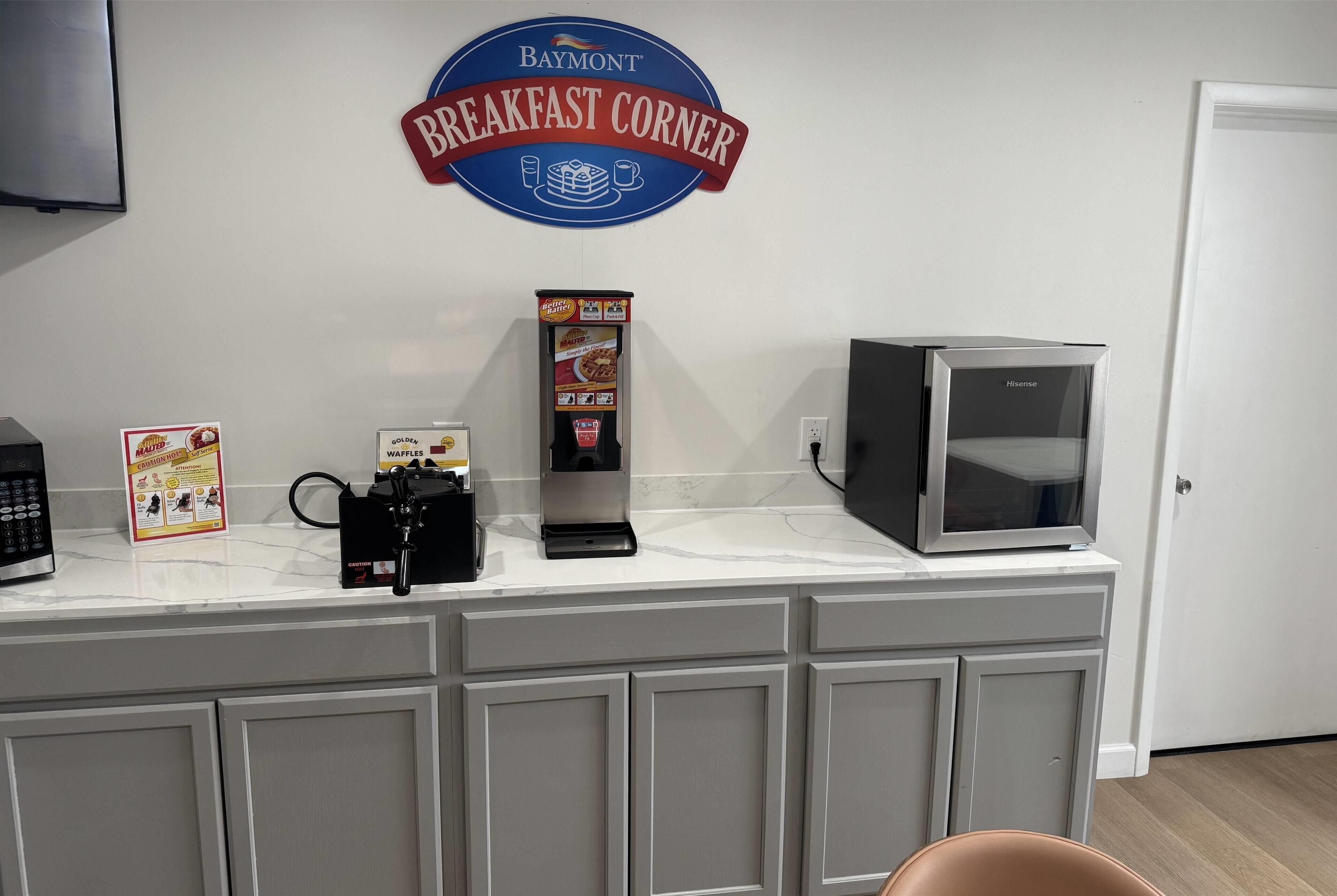Una zona de cocina con un letrero de Baymont Breakfast Corner, una máquina para gofres, una cafetera y un microondas.