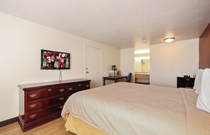 A hotel room with a large bed, a dresser, a television mounted on the wall, a desk with a chair, and a mirror.