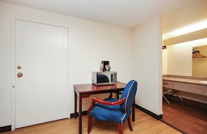 A small room with a wooden table, a microwave, a red and blue chair, a white door, and a countertop with a sink and a mirror. - Red Roof Inn Lompoc (Lompoc)