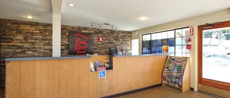 A reception desk with a Red Roof Inn sign, a fire extinguisher, and a window with blinds.