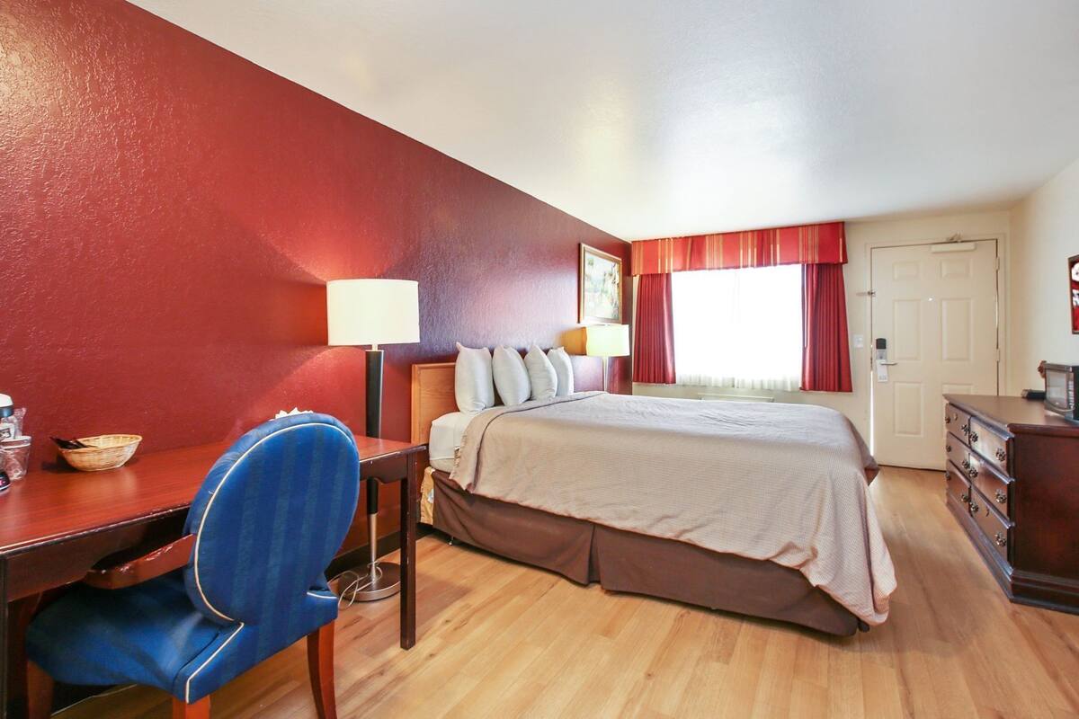 Ett hotellrum med en säng, ett skrivbord, en stol, en lampa och en tv.