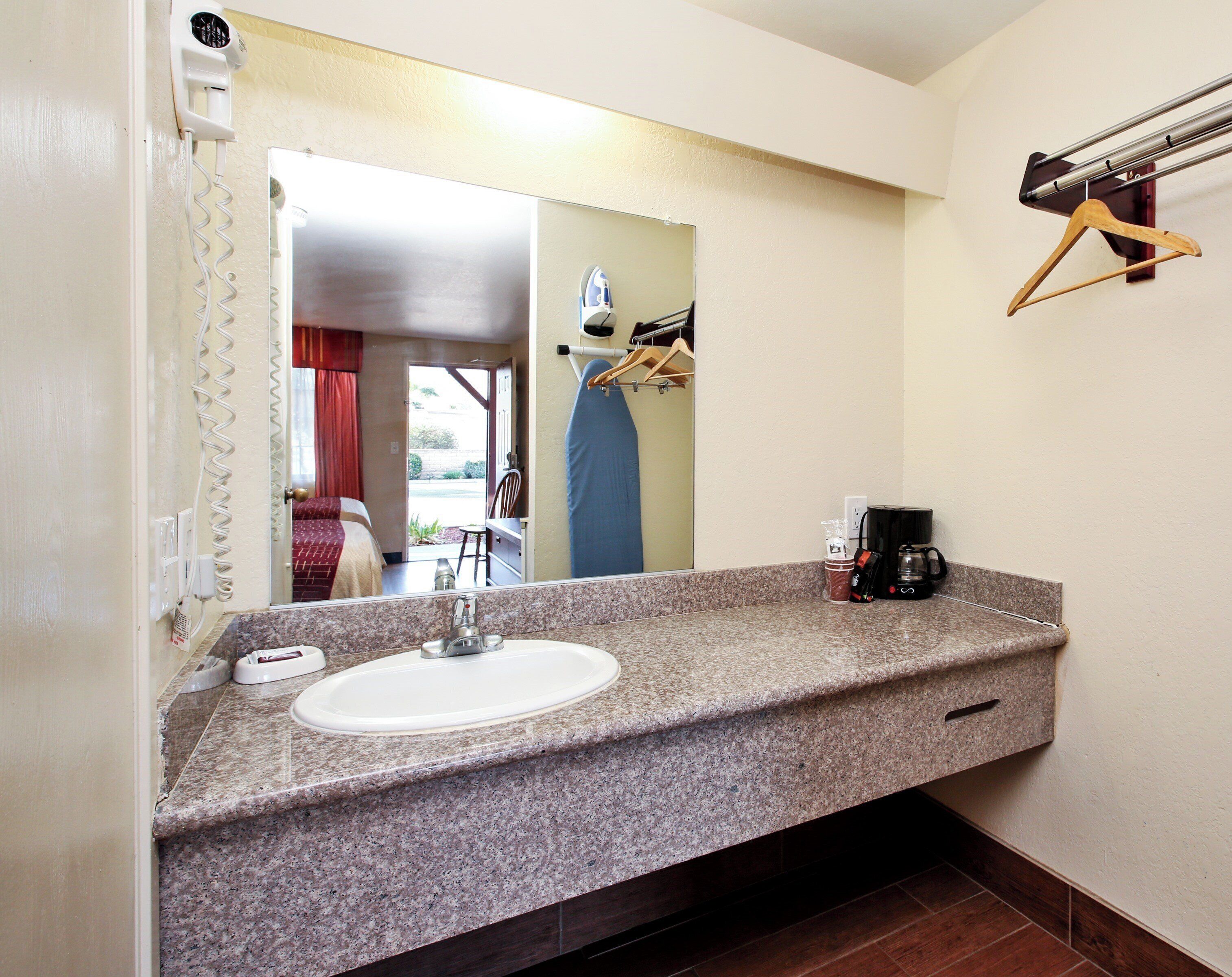 A bathroom with a granite countertop, a sink, a mirror, and a coffee maker.