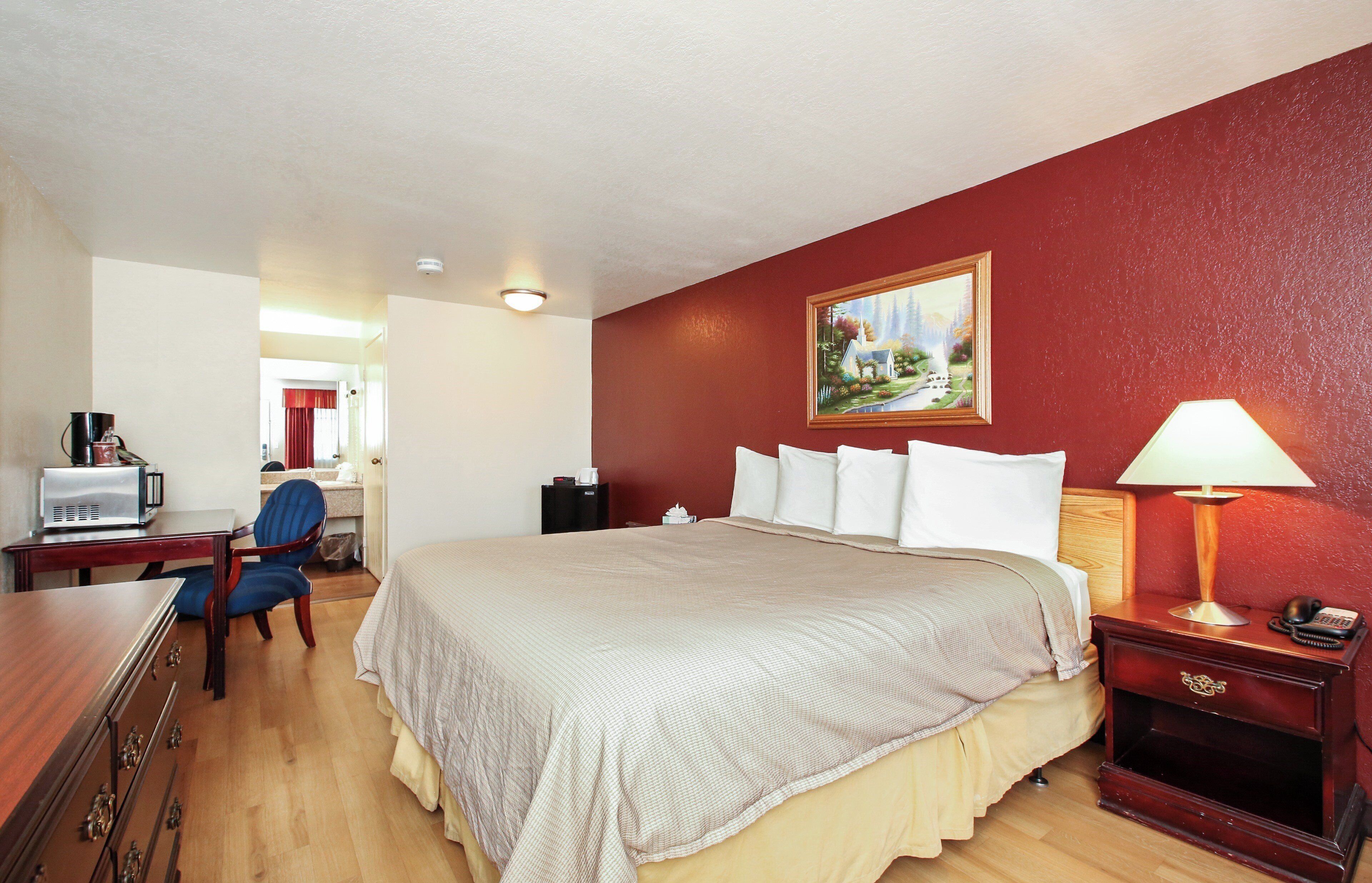 Una habitación de hotel con cama, escritorio, silla y un cuadro en la pared.