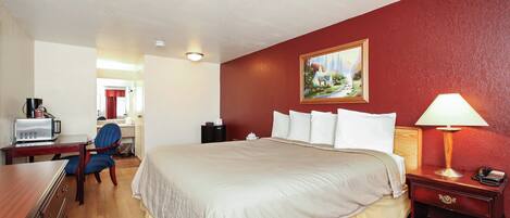 Una habitación de hotel con cama, escritorio, silla y un cuadro en la pared.