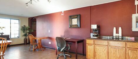 A dining area with a wooden table and chairs, a coffee station with a coffee maker and cups, and a wall clock.