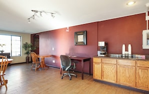 A dining area with a wooden table and chairs, a coffee station with a coffee maker and cups, and a wall clock.