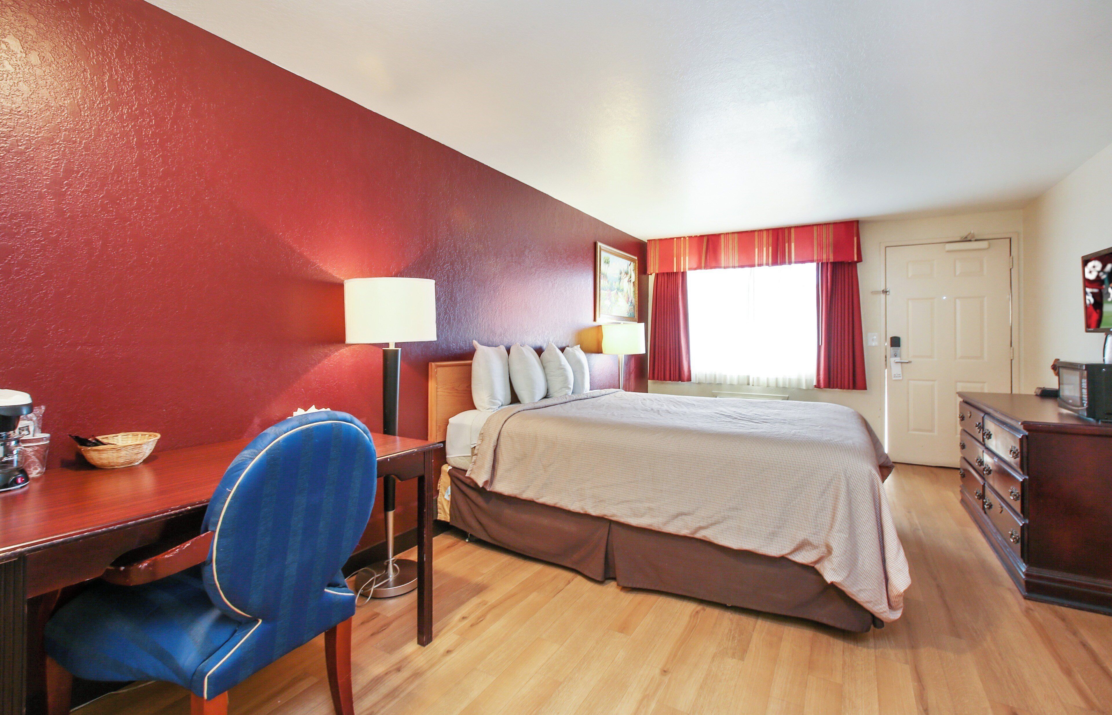 A hotel room with a bed, desk, chair, and a dresser.