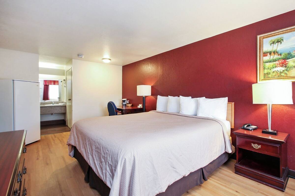 Een hotelkamer met een bed, nachtkastjes, een bureau, een stoel, een spiegel en een schilderij aan de muur.