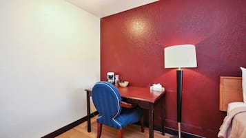 A hotel room with a desk, chair, lamp, and a red wall.