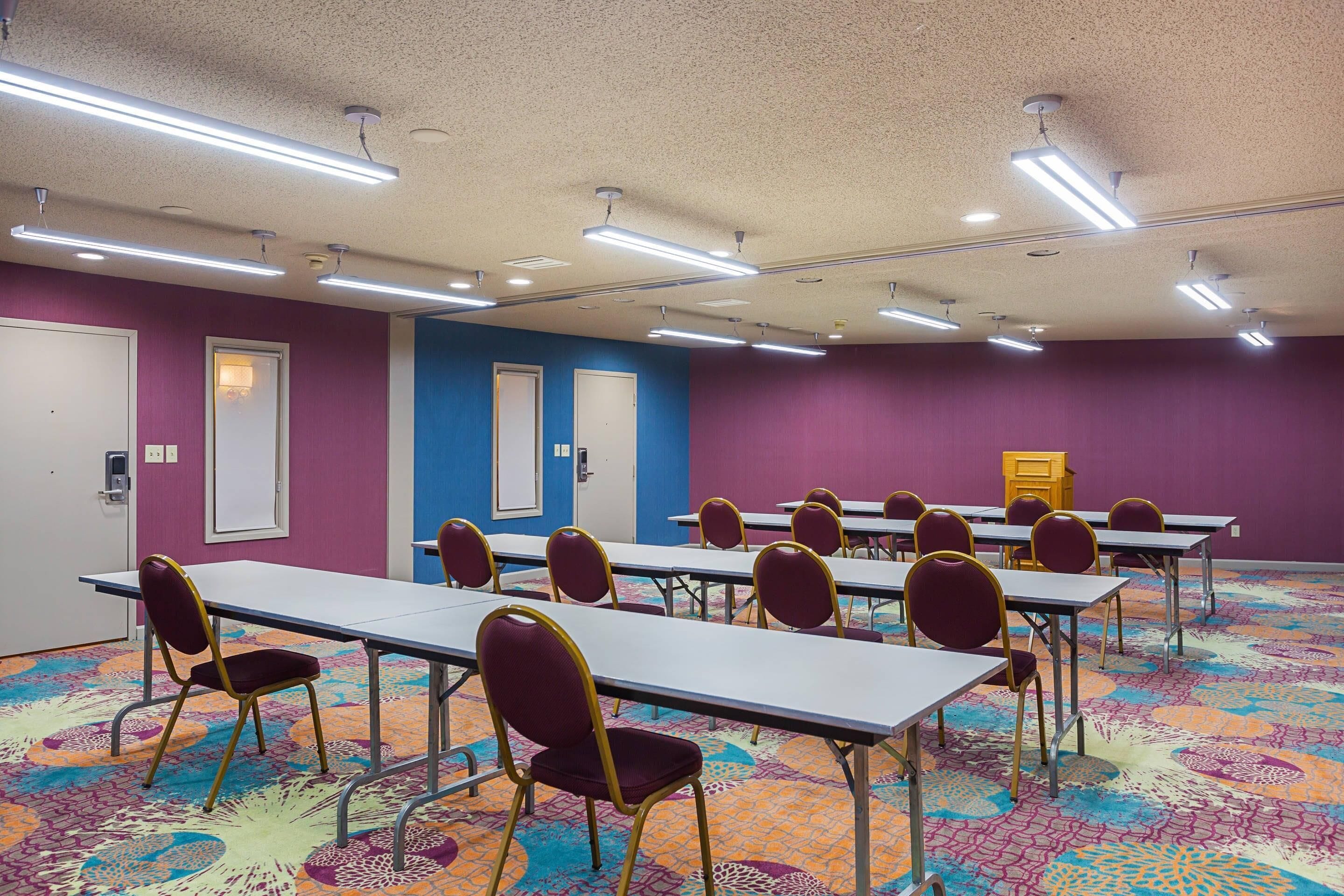 A conference room with tables and chairs, purple walls, and a patterned carpet.