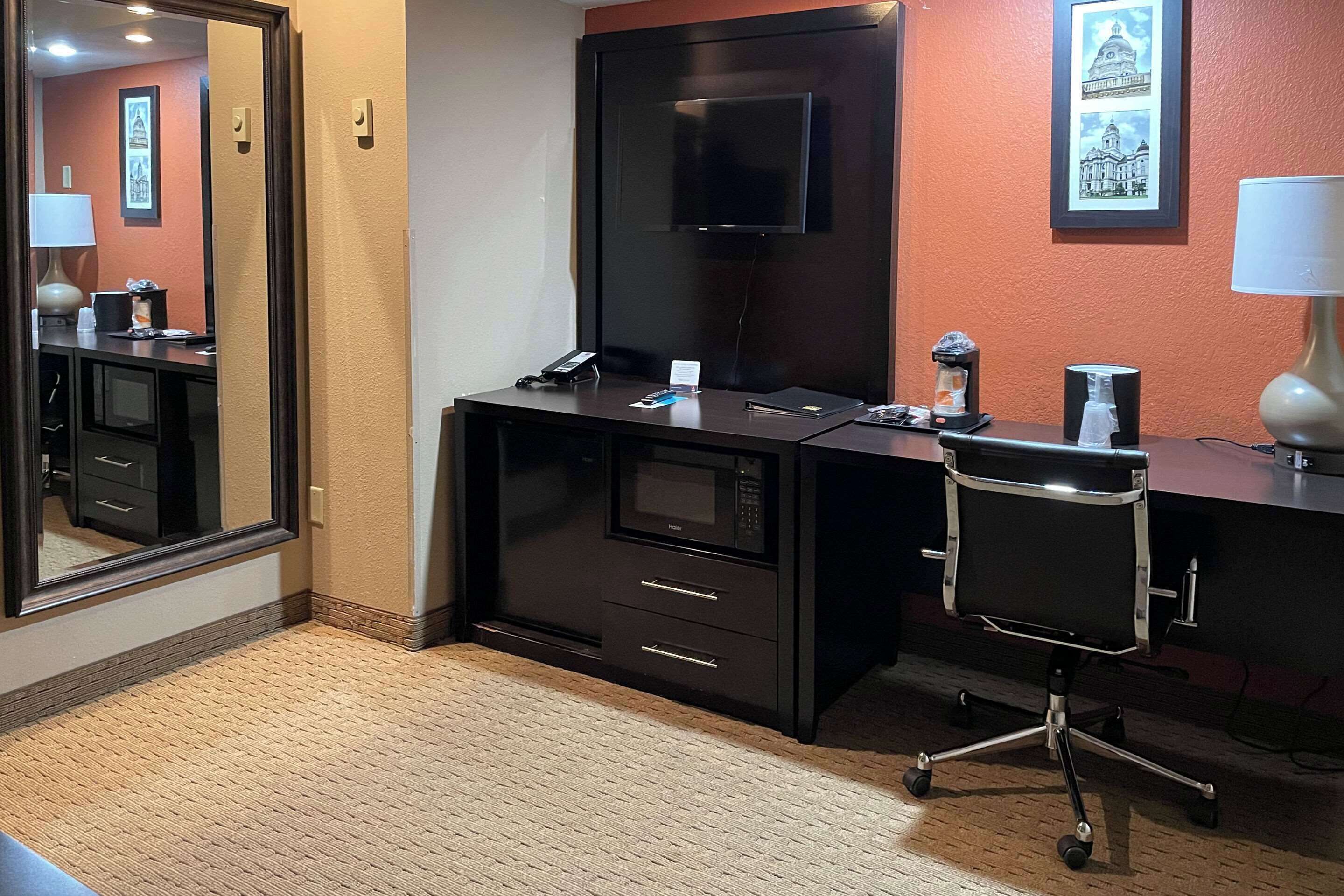Habitación de hotel con un espejo grande, un escritorio con televisor de pantalla plana, un microondas y una silla.