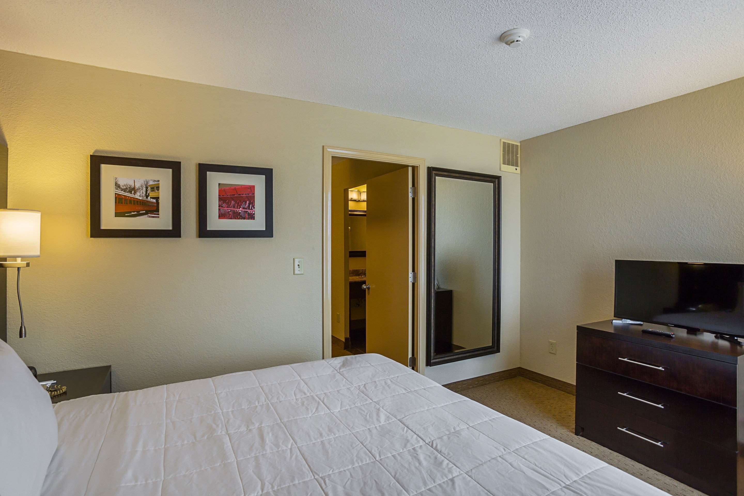 A hotel room with a bed, a dresser, a TV, and two framed pictures on the wall.