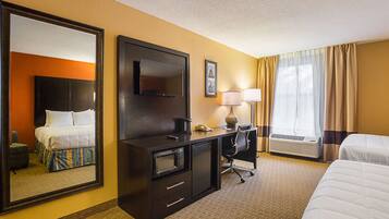Una camera d'albergo con un letto, una scrivania con un computer, una televisione e un grande specchio.
