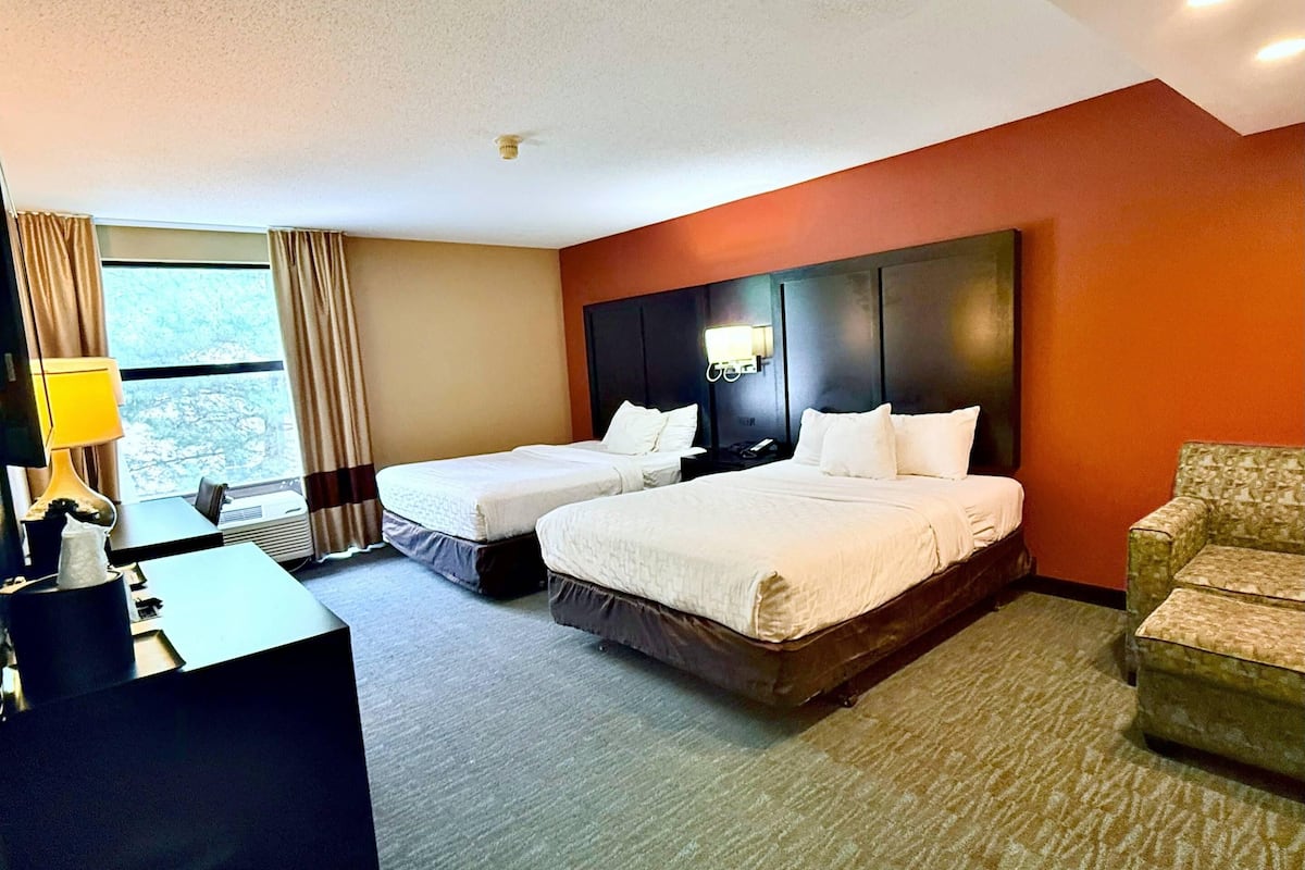 Habitación de hotel con dos camas, un escritorio, una silla y un ventanal con cortinas.