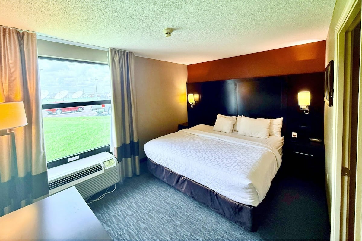 Habitación de hotel con una cama grande, un escritorio, una ventana con cortinas y vista a un estacionamiento.