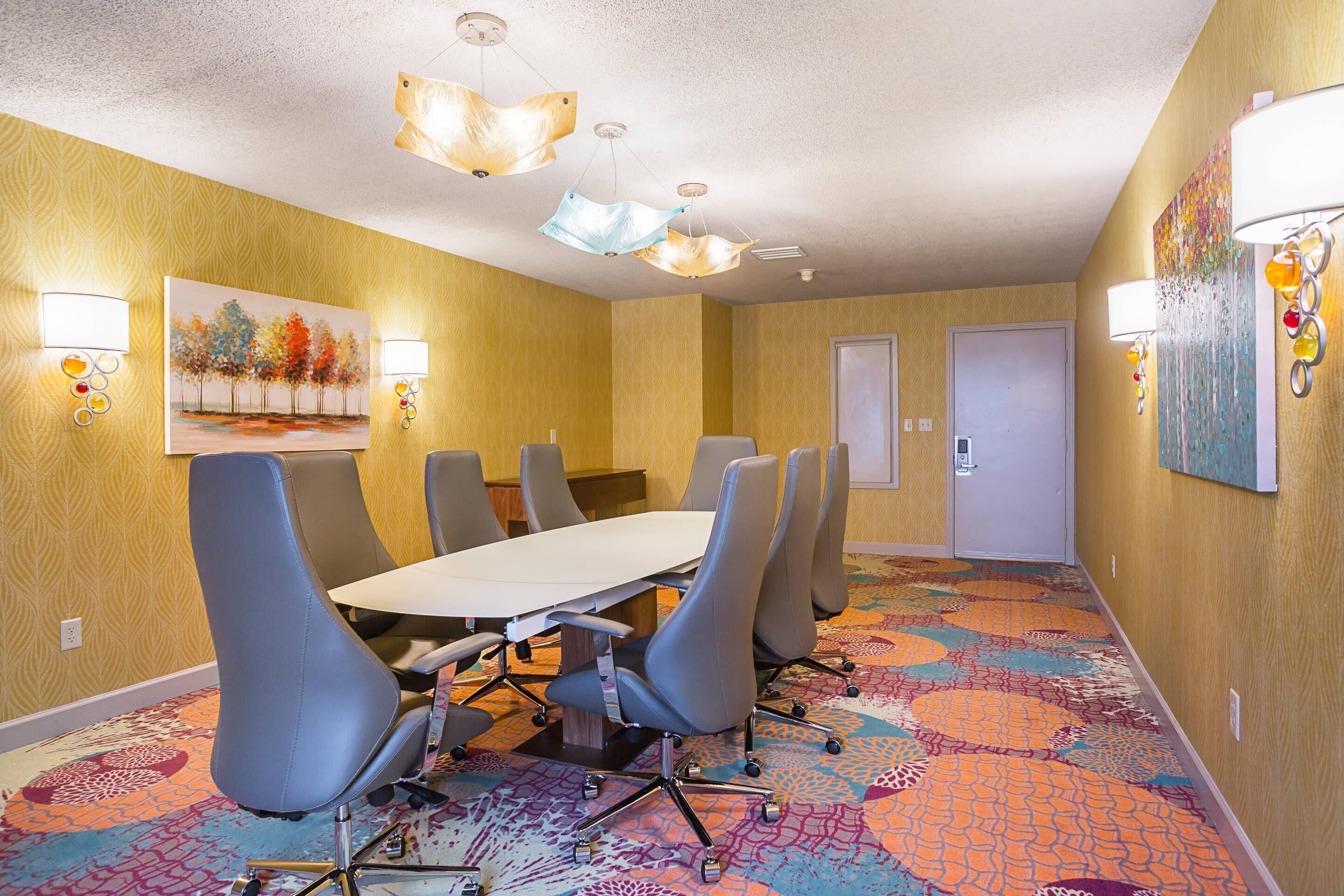 A conference room with a long table and six chairs, a patterned carpet, and wall-mounted lighting.