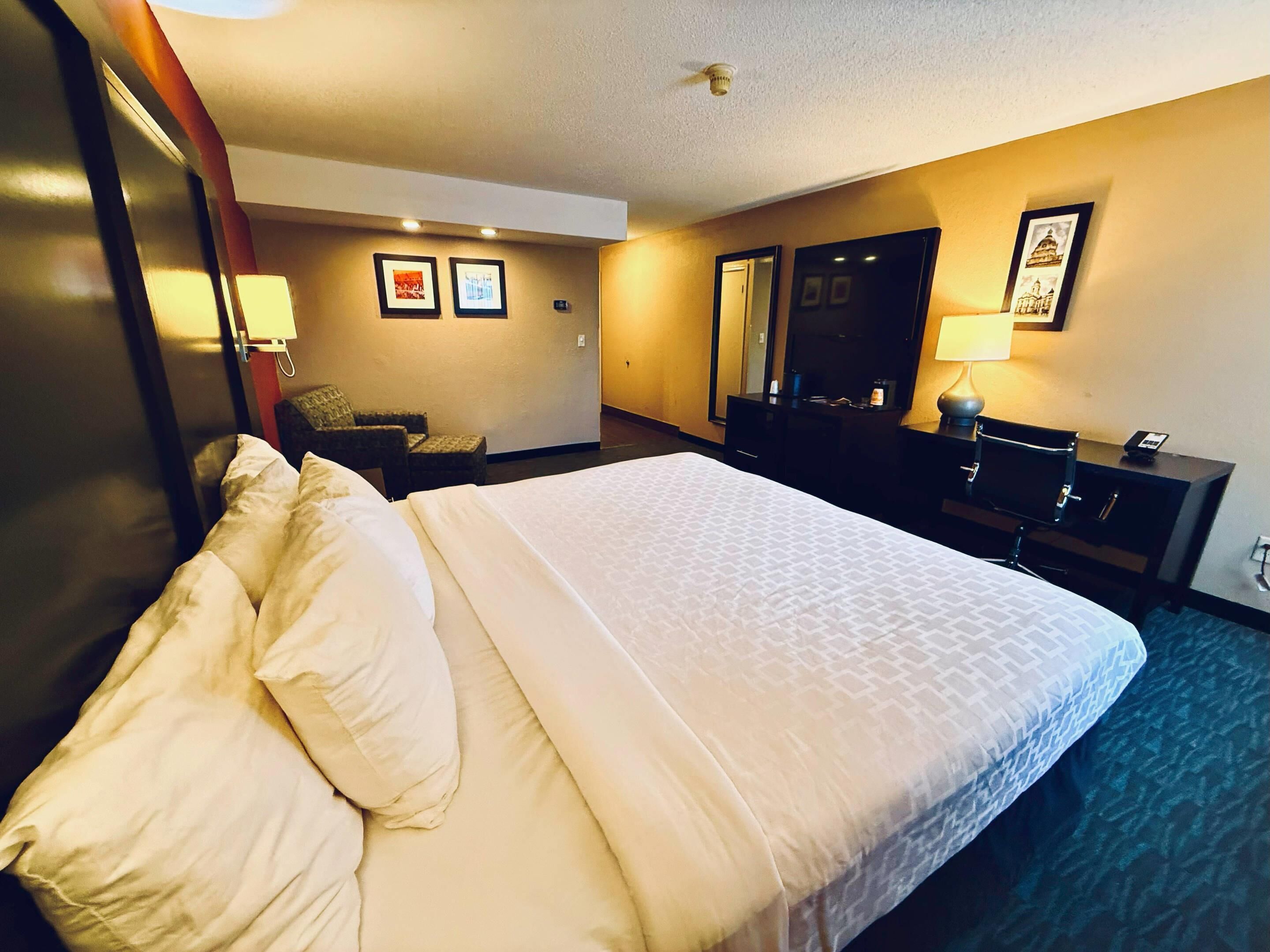 A hotel room with a large bed, a desk, a chair, a dresser, and a mirror.