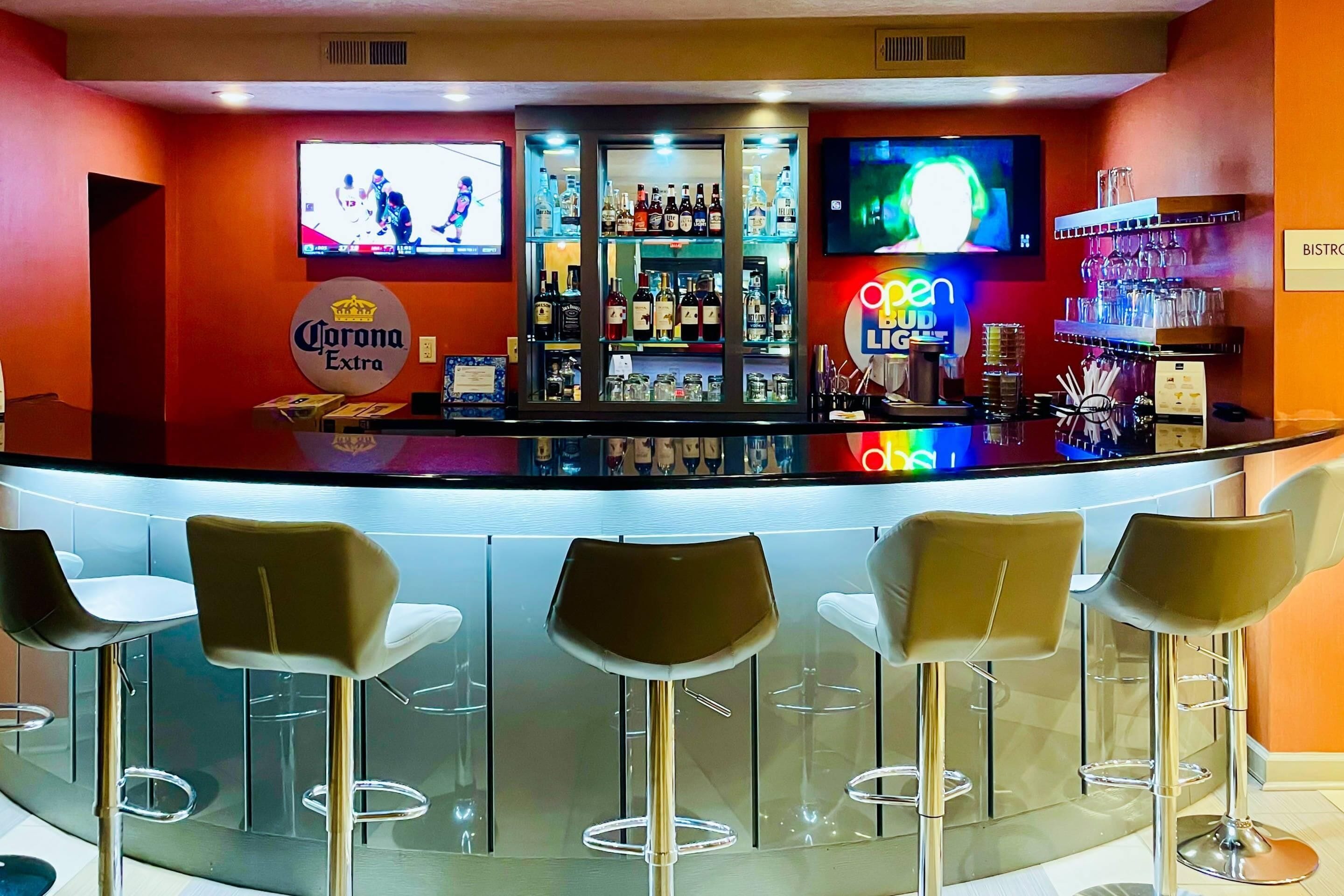 Zona de bar con un cartel de Corona Extra, una pantalla de televisión y una vitrina con botellas.