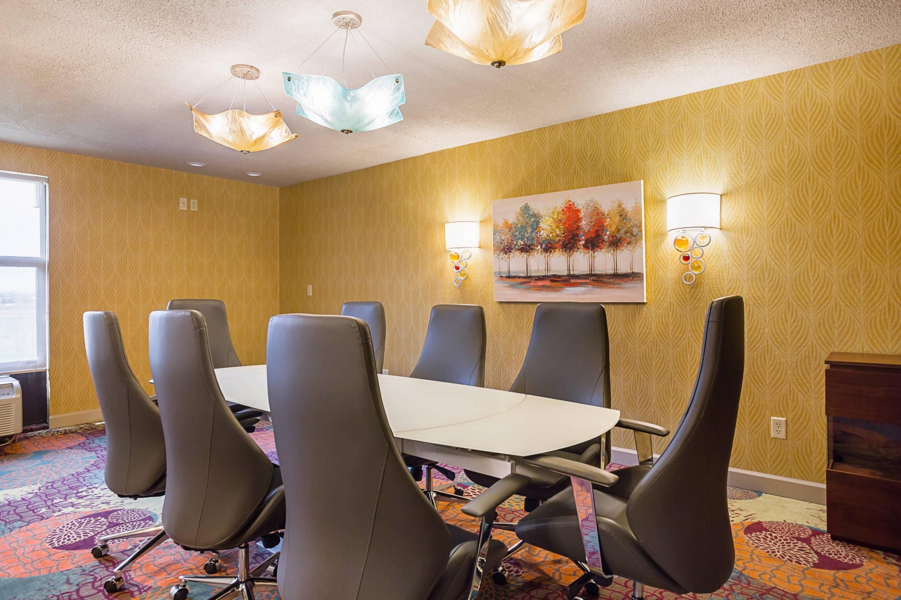 A conference room with a white table, six chairs, patterned carpet, and two wall-mounted lamps.
