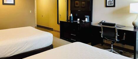 A hotel room with two beds, a desk with a chair, a television, and a mirror.