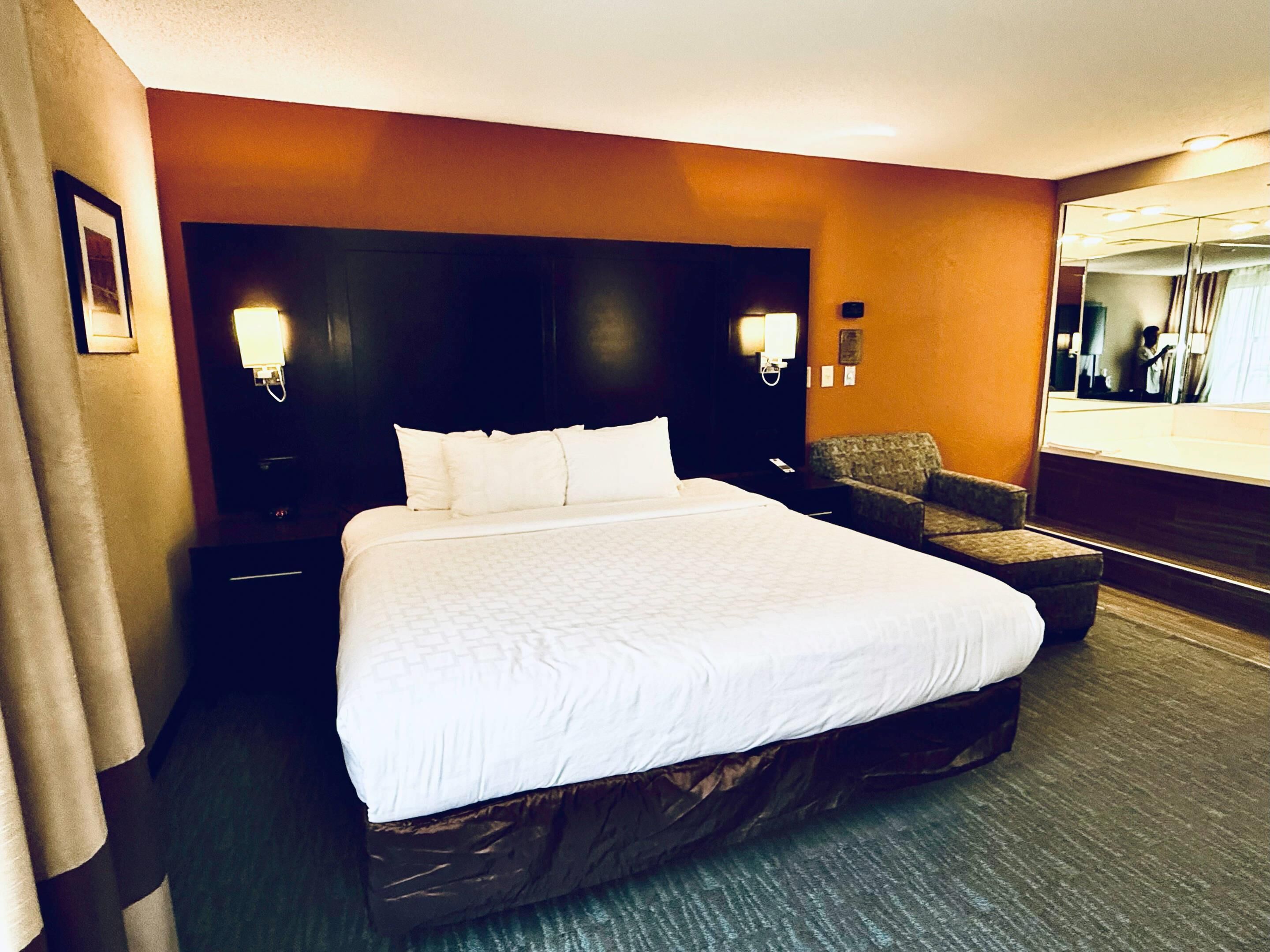 Une chambre d’hôtel avec un grand lit, deux tables de chevet, une chaise et un miroir.