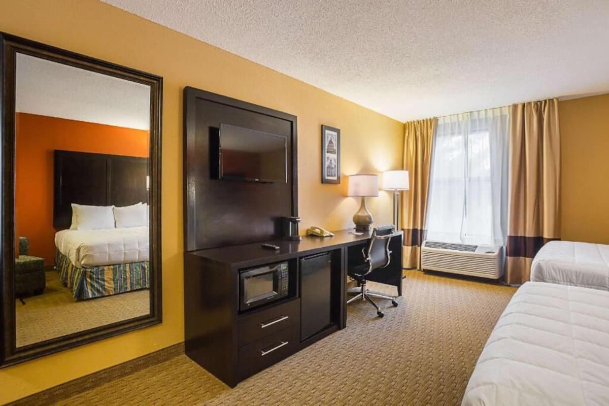 Una habitación de hotel con una cama, un escritorio con una computadora, un televisor, una lámpara y un espejo grande.