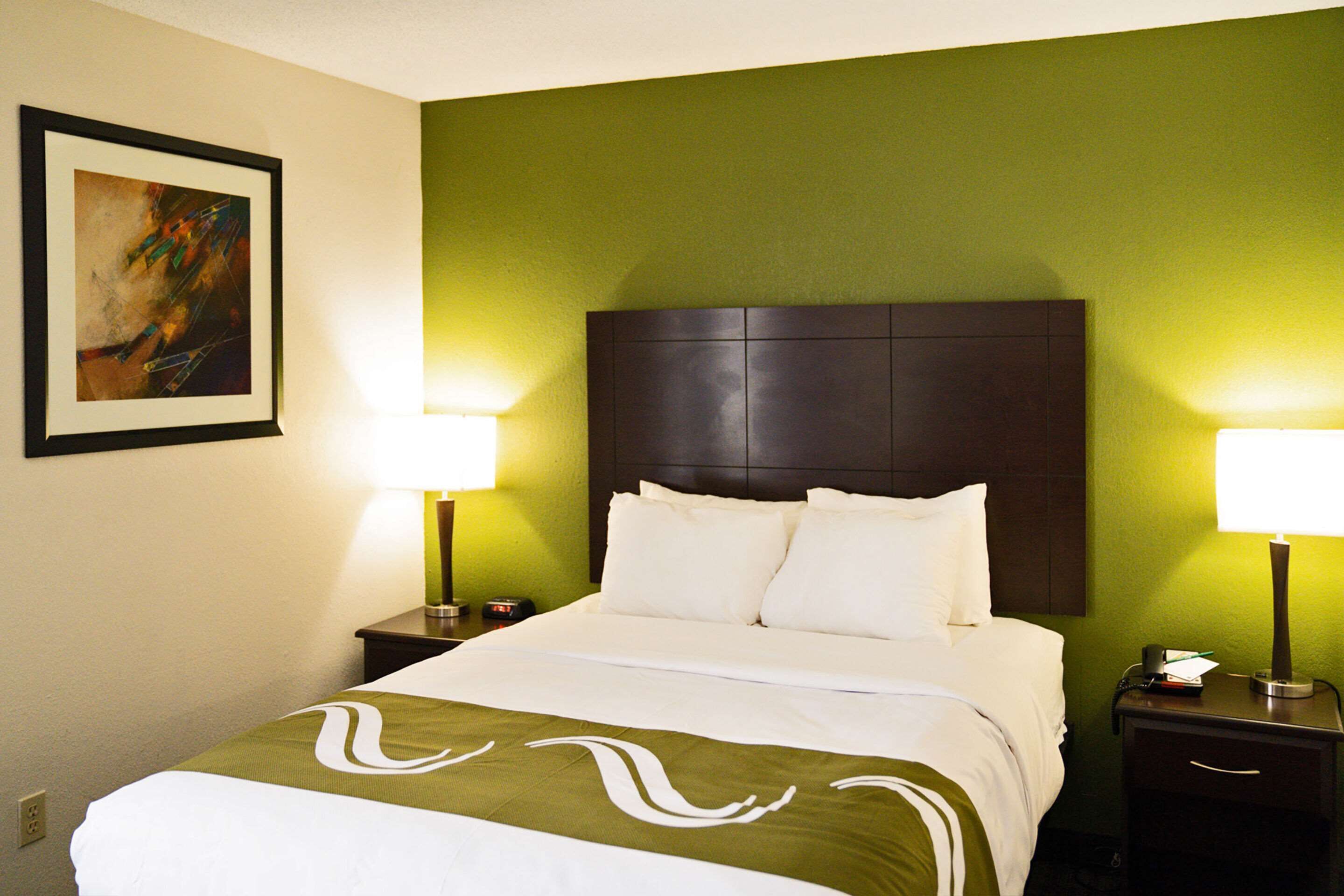 A hotel room with a large bed, green walls, two bedside tables with lamps, and a framed picture on the wall.