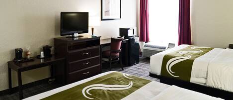 A hotel room with two beds, a desk with a television, a chair, and a window with curtains.