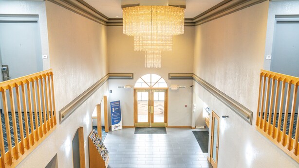 Un'hall d'albergo con un lampadario, ringhiere in legno, una reception e un'ampia porta ad arco.