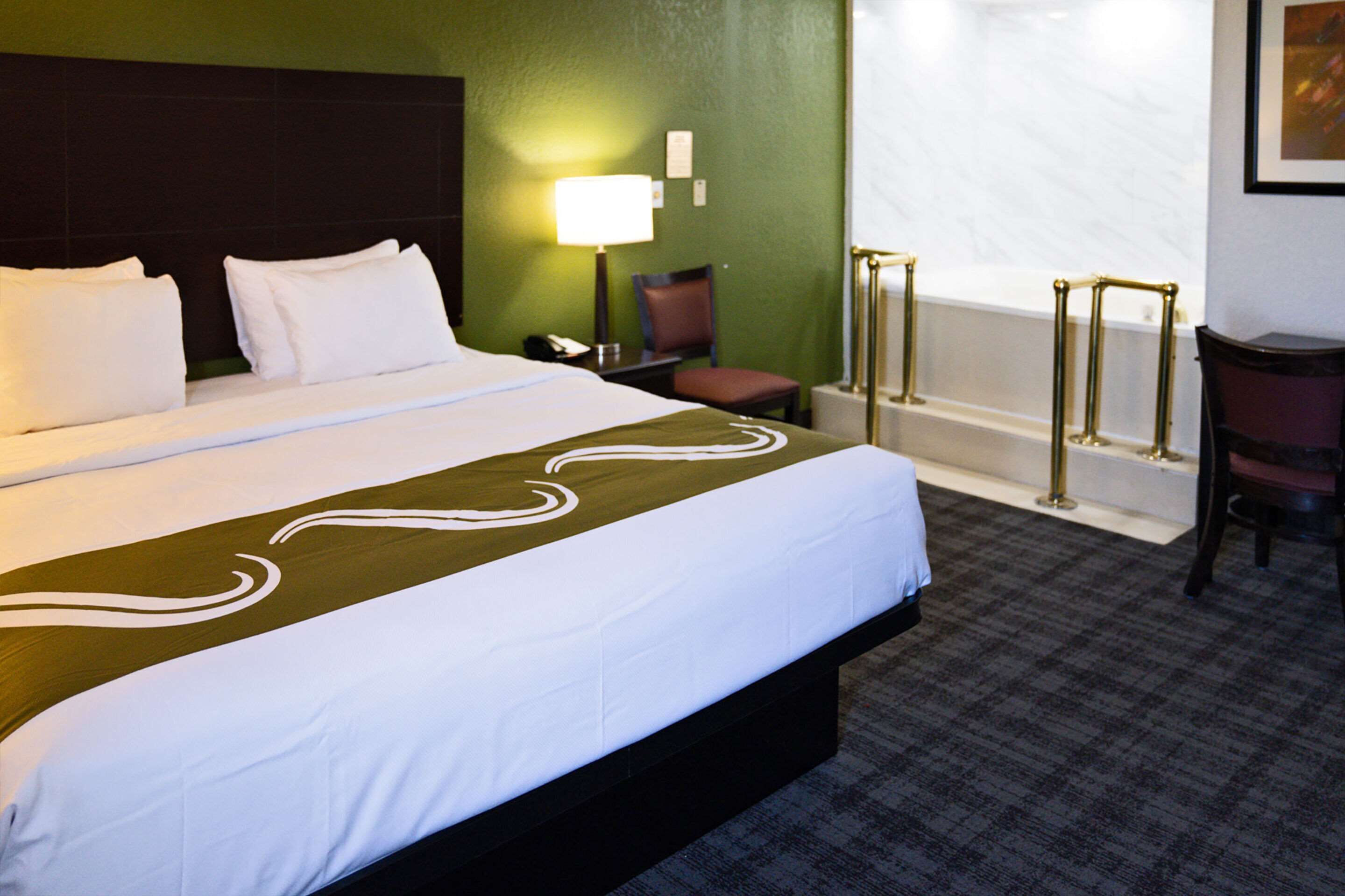 Une chambre d’hôtel avec un grand lit, une chaise, un bureau, une lampe et une baignoire.