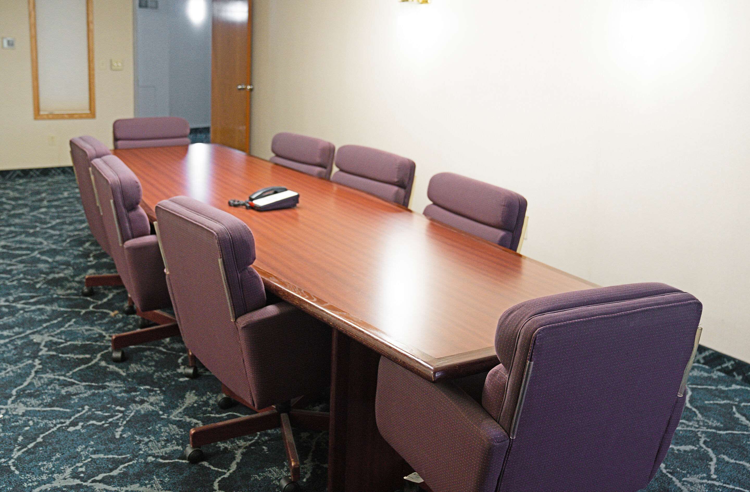 A conference room with a wooden table and six purple chairs.